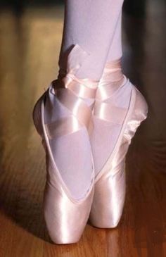 the feet of a ballerina in white ballet shoes on a wooden floor with her leg wrapped up