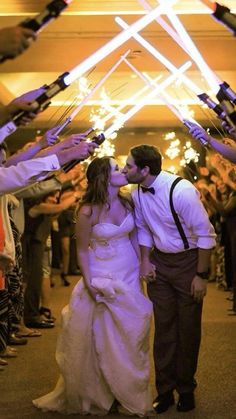 a bride and groom kissing in front of their wedding party with sparkler wands