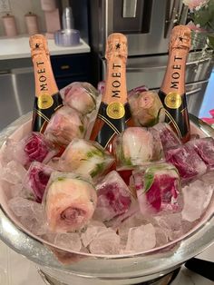 four bottles of champagne on ice in a bowl with flowers and roses around the edges