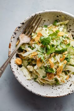 a white bowl filled with salad on top of a blue tablecloth next to a fork