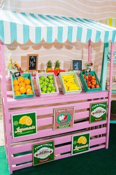 a pink fruit stand with oranges, lemons and limes on display in front of a striped wall