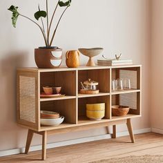 a wooden shelf with bowls and plates on it next to a plant in a vase