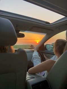 two people sitting in the driver's seat of a car as the sun sets