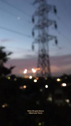 blurry photograph of power lines at night with the sky in the back ground and lights on