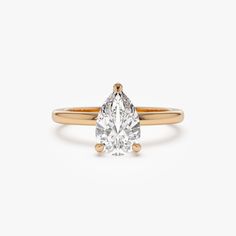 a yellow gold engagement ring with a pear shaped diamond in the center, on a white background