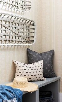 a bench with some pillows and a hat on it next to a wall mounted mirror