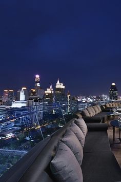 an outdoor seating area with city lights in the background at night, along with couches and tables