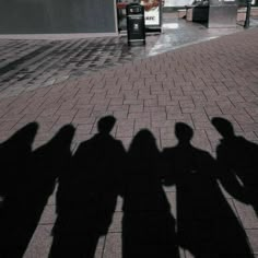 the shadow of three people standing next to each other on a brick walkway in front of a building