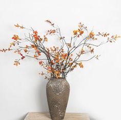 a vase filled with flowers sitting on top of a wooden table next to a white wall