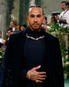 a man in a black suit with his hands on his chest and wearing a gold chain around his neck