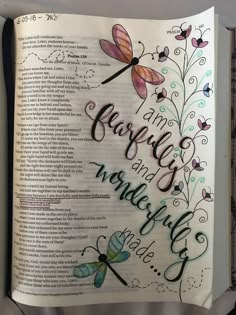 an open bible with dragonflys and flowers on it's page, which is written