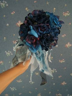 a hand holding a bouquet of blue and purple flowers in it's left arm