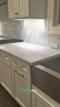 a kitchen with white cabinets and gray counter tops, an island sink and stainless steel dishwasher