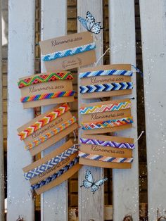 several colorful bracelets hanging on a white wooden fence with butterflies flying above them in the background