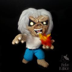 a crocheted troll with white hair and blue pants holding a fire in its mouth