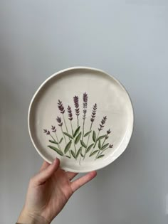 a hand holding a white plate with purple flowers on it