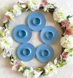 four blue dishes sitting on top of a table surrounded by white and pink flower wreaths