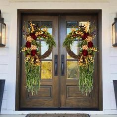 two wreaths on the front door of a house decorated with flowers and greenery