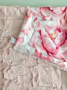 a pink flowered blanket laying on top of a bed next to a black and white dice