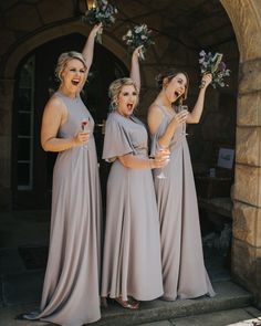 three bridesmaids in grey dresses holding bouquets and waving at the camera with their hands up