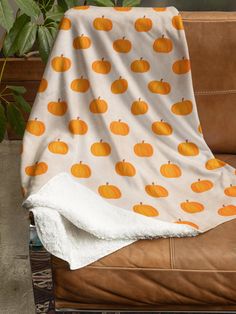 an orange pumpkin pattern on a white blanket sitting on top of a brown leather couch