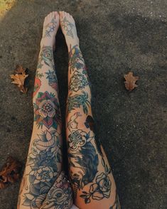 a woman's legs with tattoos on them sitting on the ground next to leaves