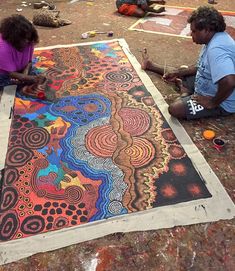 two people sitting on the ground working on an art project