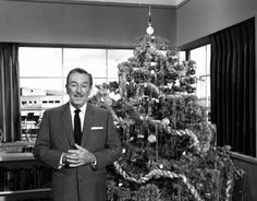 a black and white photo of a man standing in front of a decorated christmas tree