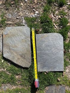 two pieces of slate laying on the ground next to a measuring tape and some rocks