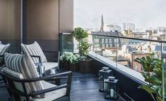 a balcony with chairs and plants on the top floor, overlooking cityscape in the distance