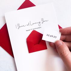 a hand holding a red envelope with a heart on it and a card that says, i year of loving you happy anniversary