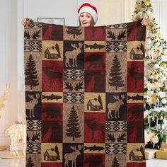 a woman is holding up a quilt with moose and trees on it in front of a christmas tree