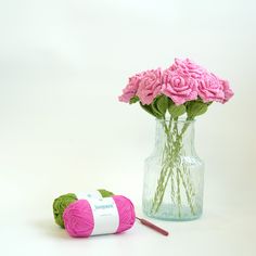 pink flowers in a vase next to a crochet hook and ball of yarn