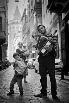 a man holding an accordion while standing next to a little boy on a brick street