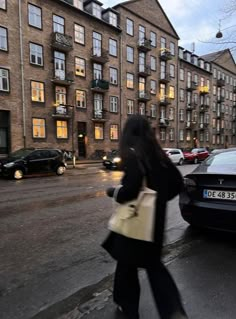 a woman is walking down the street in front of some tall buildings with many windows