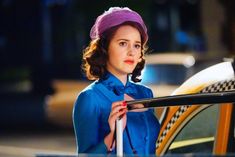 a woman standing next to a taxi with a hat on her head and holding a cane