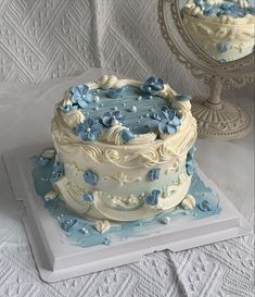 a white and blue cake sitting on top of a table next to a mirror,