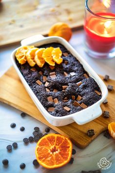 an orange and chocolate cake in a baking dish on a cutting board next to sliced oranges