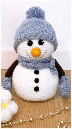 a crocheted snowman with a hat and scarf sitting next to a flower