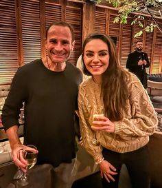 a man and woman standing next to each other holding wine glasses in front of them