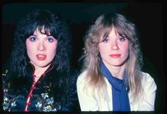 two women in jackets and ties posing for the camera with one woman's face partially obscured by her hair