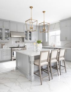 an instagram photo of a kitchen with gray cabinets and white marble countertops, gold pendants over the island