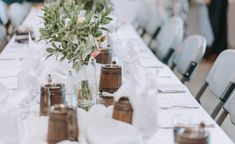 the table is set up with white linens and wooden vases filled with flowers