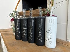 four personalized stainless steel flasks sitting on top of a wooden table in front of a fireplace