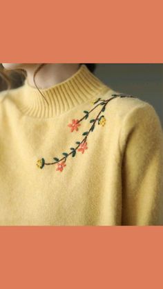 a woman wearing a yellow sweater with flowers embroidered on the front and sides, looking down at her left shoulder