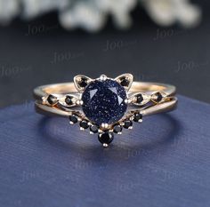 a gold ring with a blue stone surrounded by black diamonds on top of a blue cloth