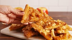 a person holding up some food on top of a cutting board next to an apple