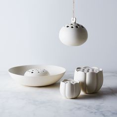 three white bowls and one bowl with holes in the middle on a marble countertop