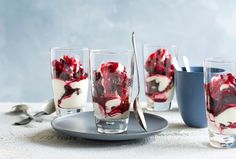 three glasses filled with dessert sitting on top of a table next to cups and spoons