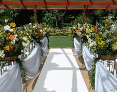 an outdoor ceremony with white linen draped over the aisle and flower arrangements on either side